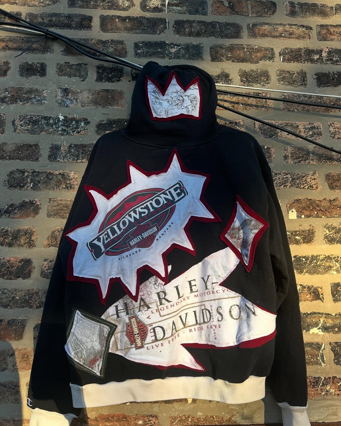 Back of the black Harley hoodie, Yellowstone tee scraps stitched into a starburst, hanging on a brick wall